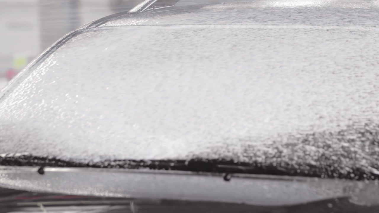 Autolavaggio al rallentatore con sapone spray schiumogeno applicato sul parabrezza dell'auto