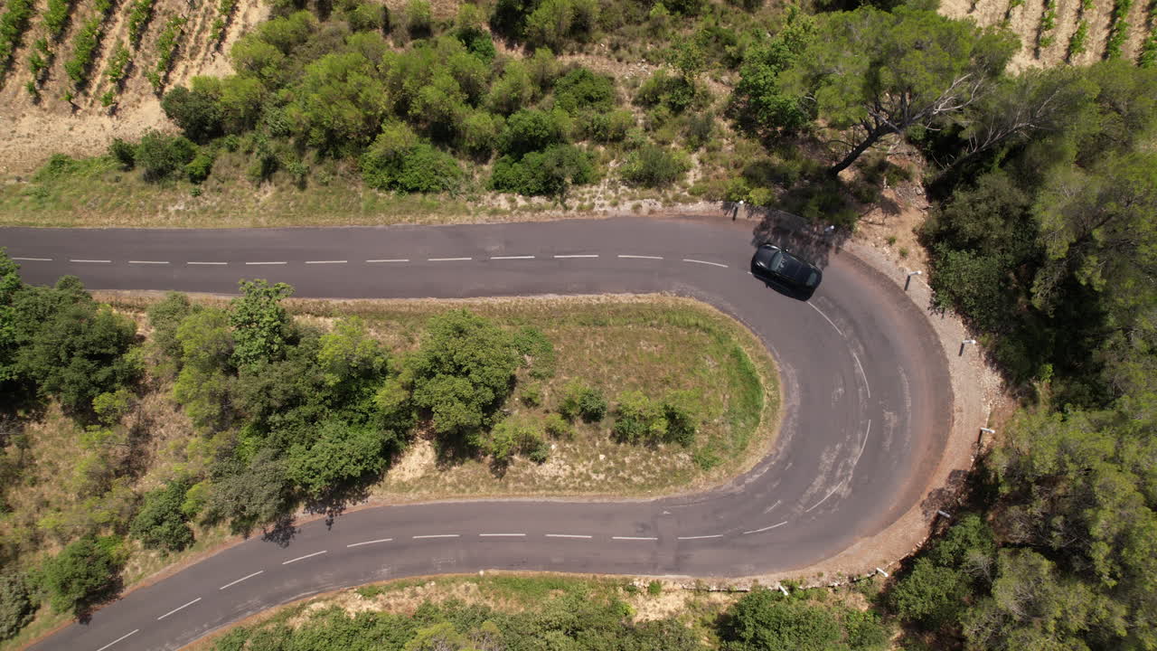 Tomada aérea superior sobre uma estrada sinuosa com carro elétrico passando no Sul da França