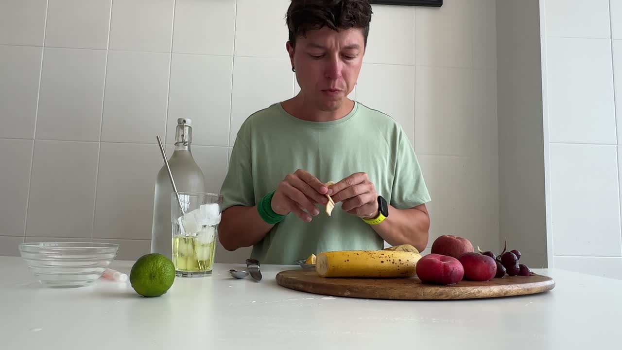 Uomo che Mangia e Prepara Frutta Fresca in una Cucina Luminosa