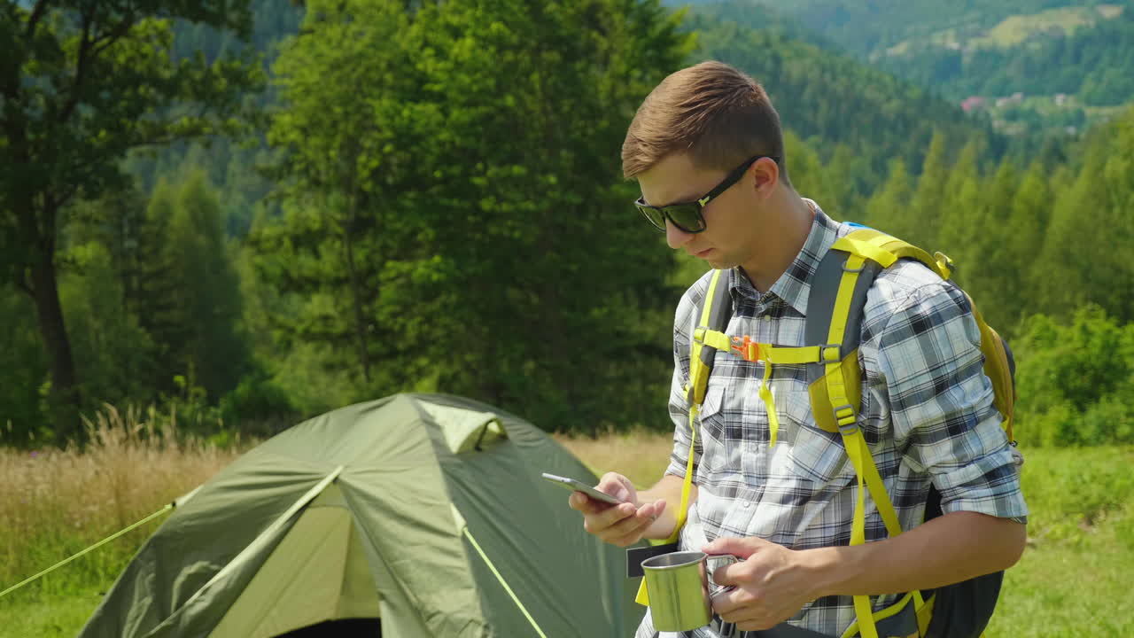 un joven con una mochila usa un teléfono inteligente en la aplicación de camping siempre en contacto para el turismo