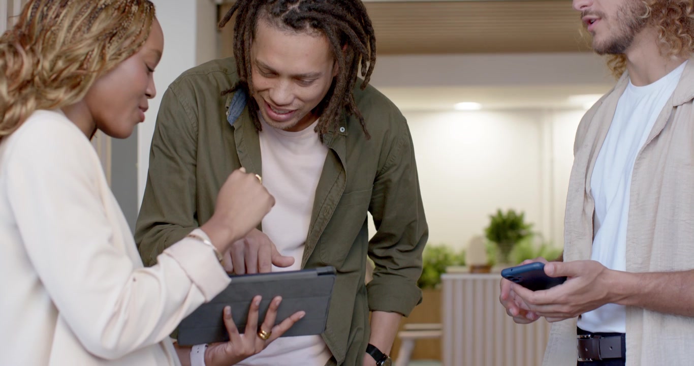 Diverse team at work reviewing tablet, woman blazer tapping, man holding phone pointing, confirming