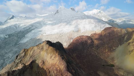 high altitude aerial pan left across the rugged paso del zorro in peru’s cordillera blanca, revealing colorful peaks, glacial snow, and dramatic andean scenery