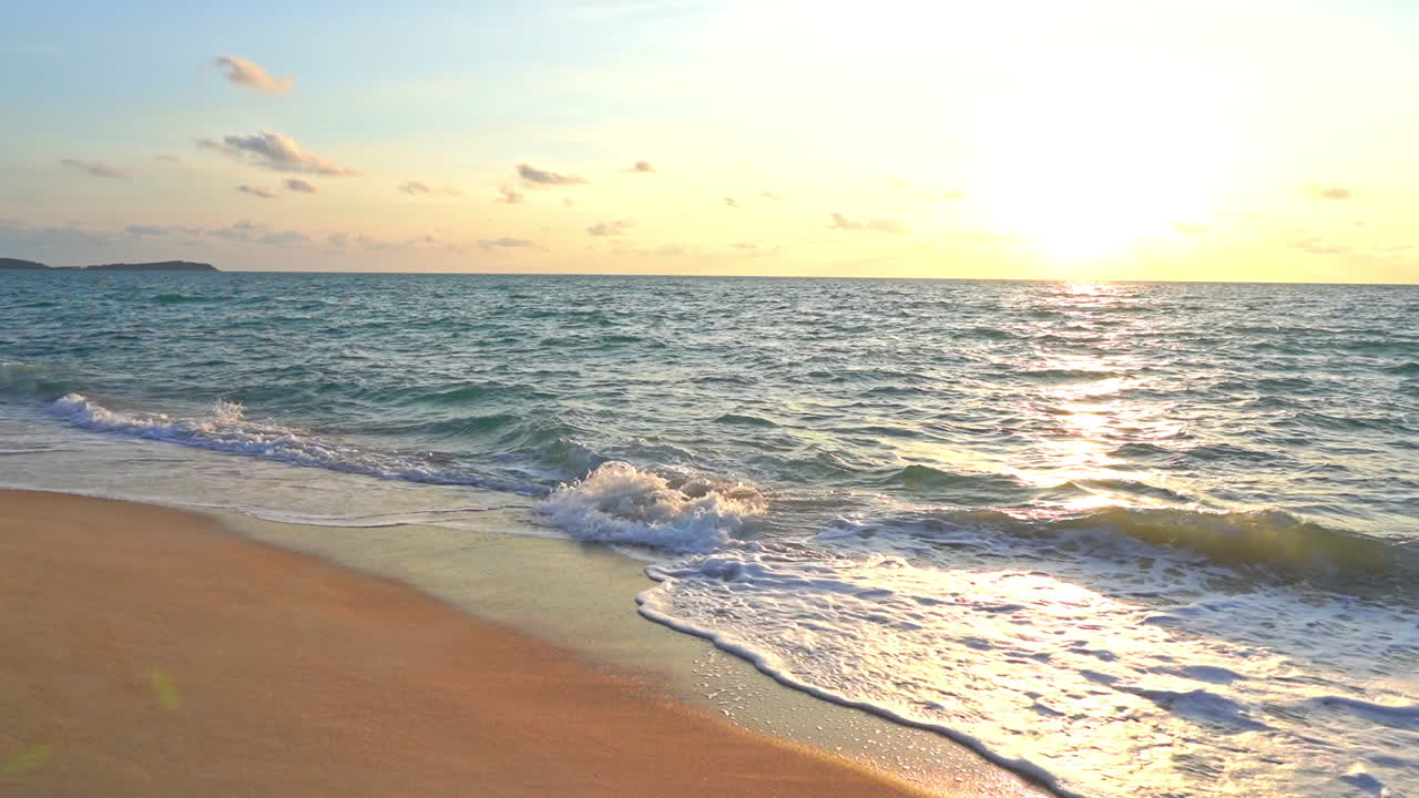 Slow-motion waves wash up on a deserted tropical beach under a setting sun