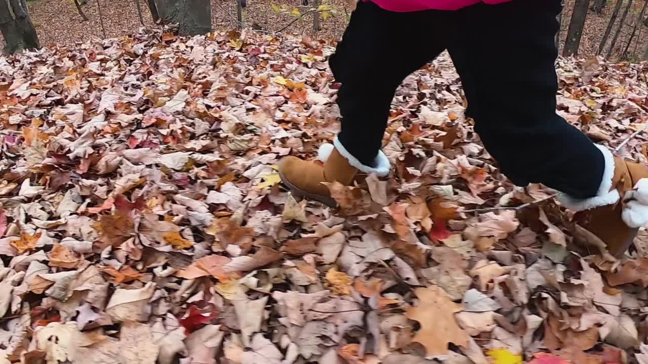 Close up of little girl's leather boots with faux fur as she runs through an autumn forest SLOW MOTION
