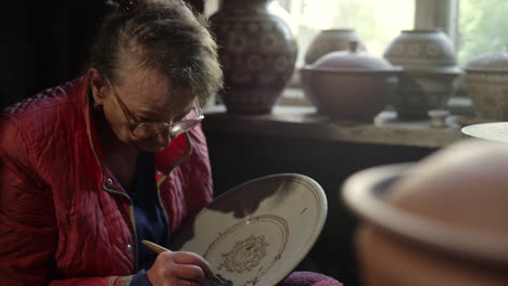 serious old woman decorating plate in pottery