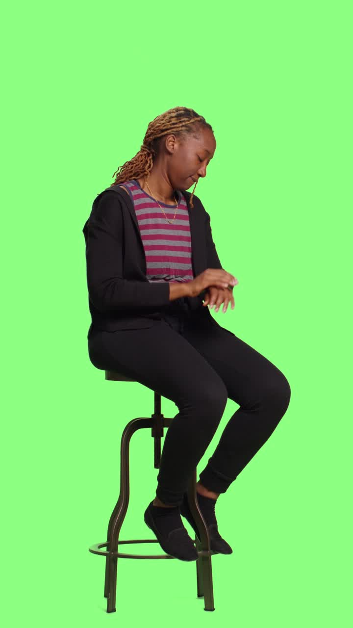 Video verticale: persona afroamericana seduta su una sedia su greenscreen integrale