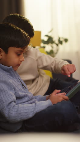 Video-Vertical-De-Dos-Niños-Pequeños-Sentados-En-Un-Sofá-En-Casa-Jugando-O-Transmitiendo-Juntos-A-Una-Tableta-Digital