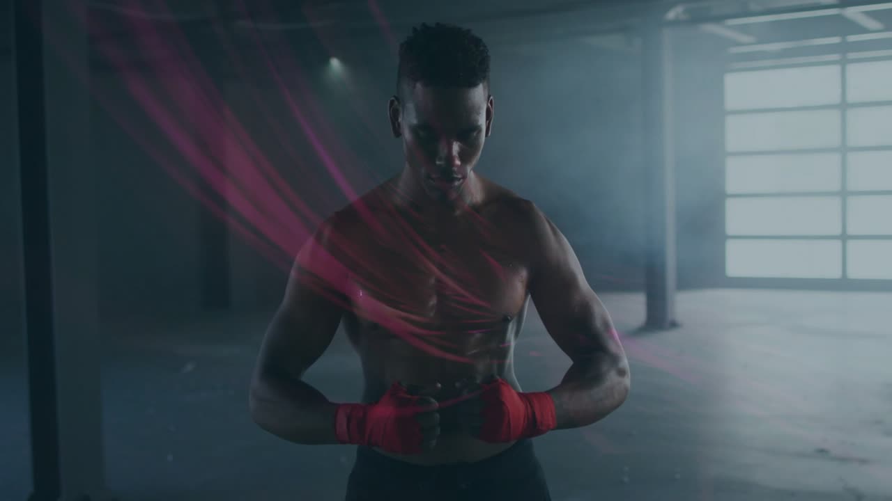 Boxer looking down tying red wraps in warehouse prepping for boxing as pink streaks sweeping torso