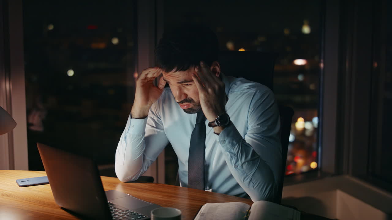 Empleado profesional frustrado trabajando hasta tarde en la noche en una oficina oscura. Hombre cansado