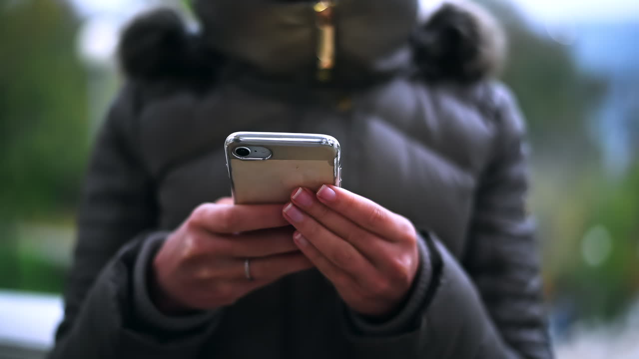 Una persona sta usando uno smartphone all'aperto, di sera. Indossa una giacca pesante ed è circondata da un tranquillo ambiente esterno.
