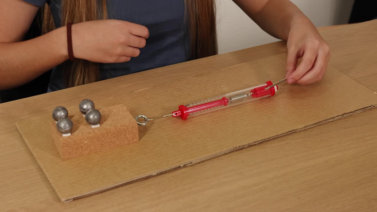 A person uses a spring scale to measure force needed to drag weights on cardboard, illustrating friction principles