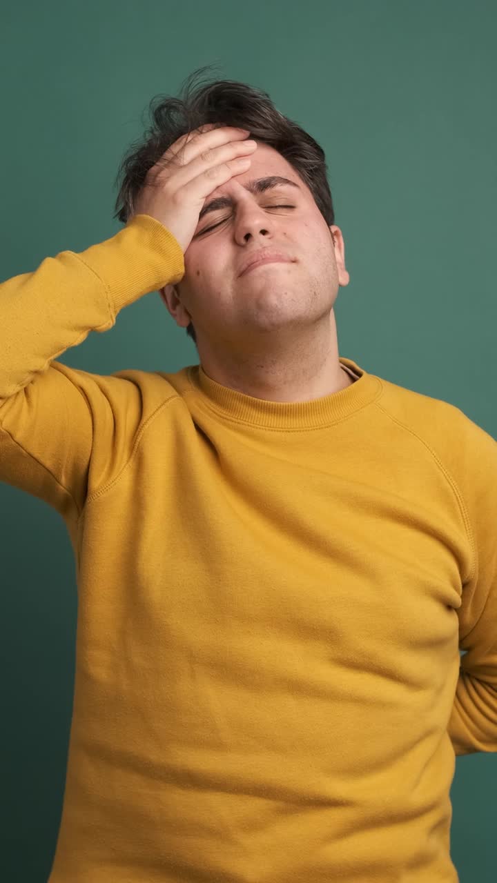 Frustrated man suffering from headache in green studio