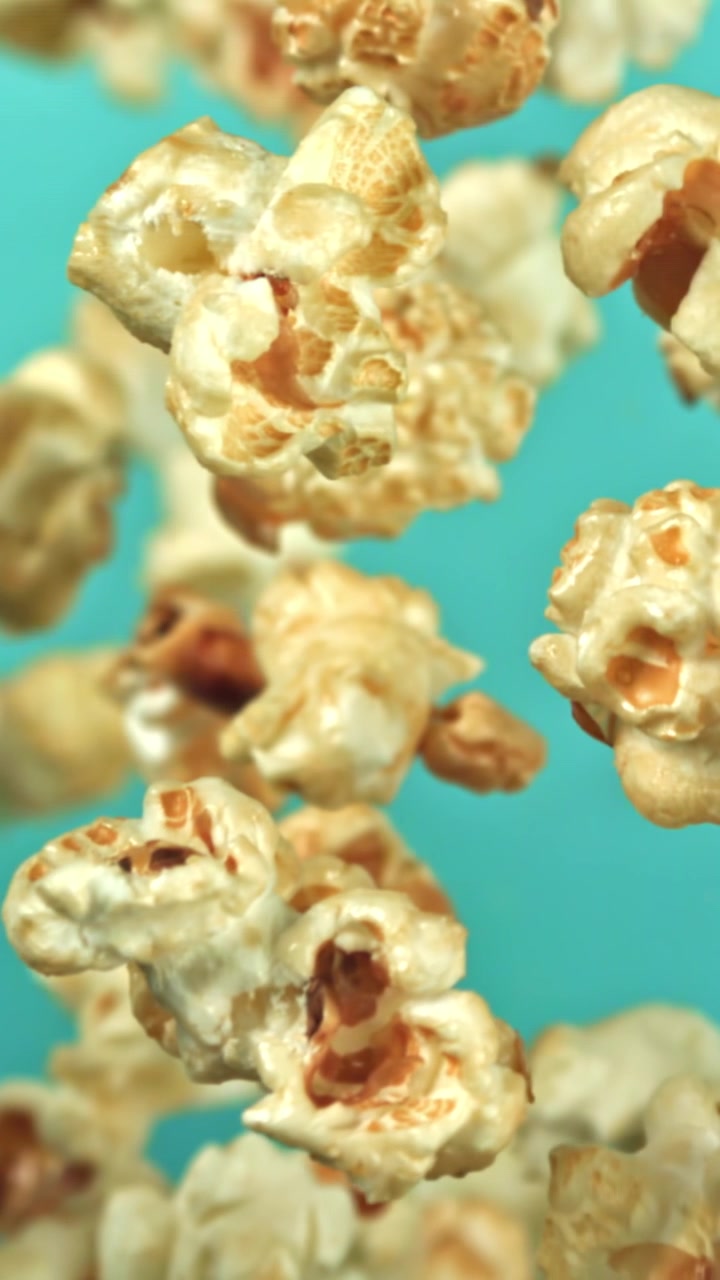 Deliziosi chicchi di popcorn che fluttuano al rallentatore su uno sfondo blu