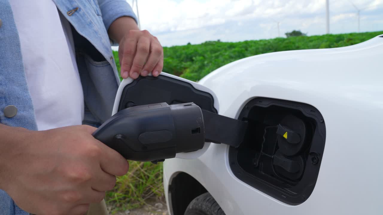 hombre con su coche eléctrico y su turbina eólica como concepto progresivo de energía renovable.