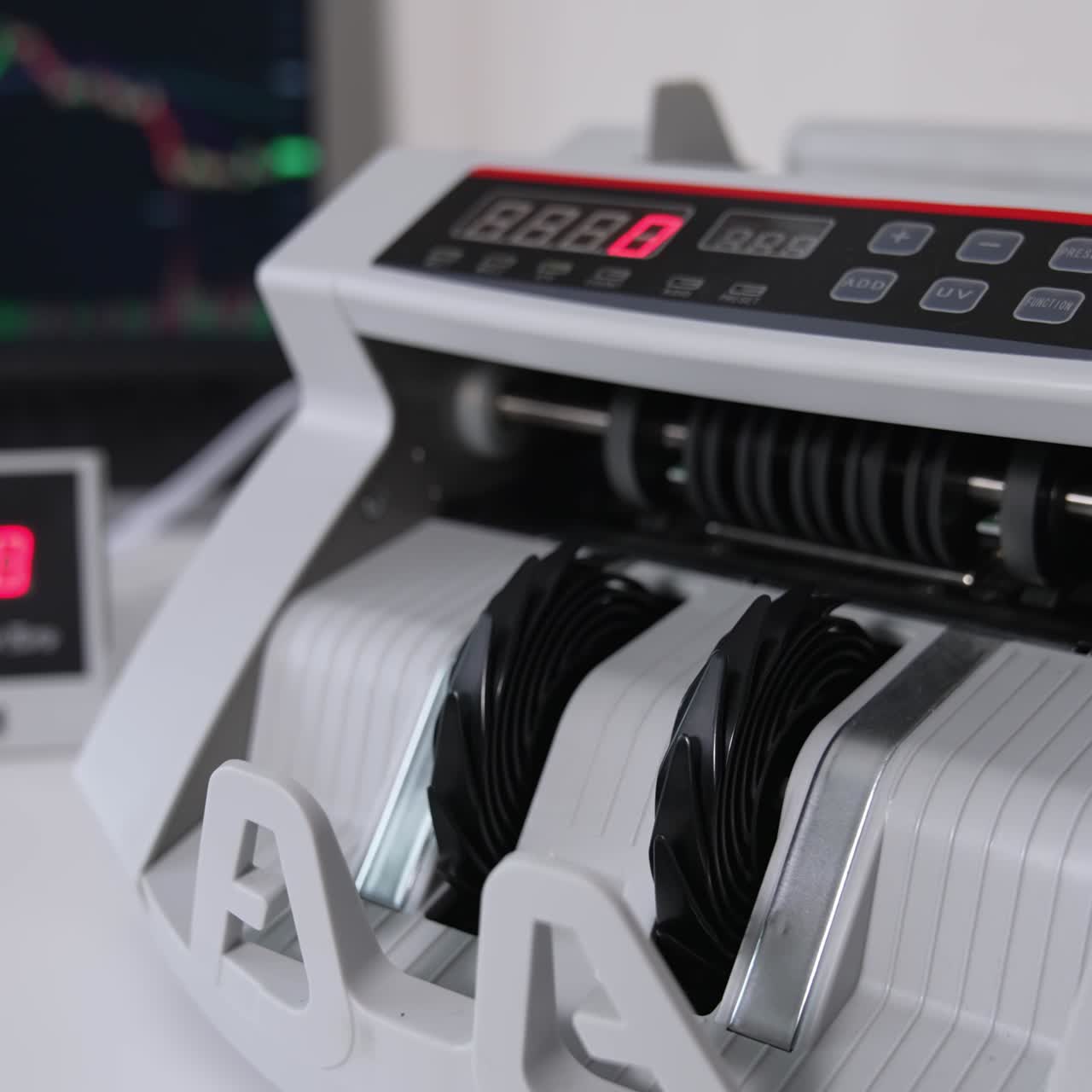 Money counting machine with a wad of fifty euro banknotes. Close up. Laptop opened at backdrop in blur