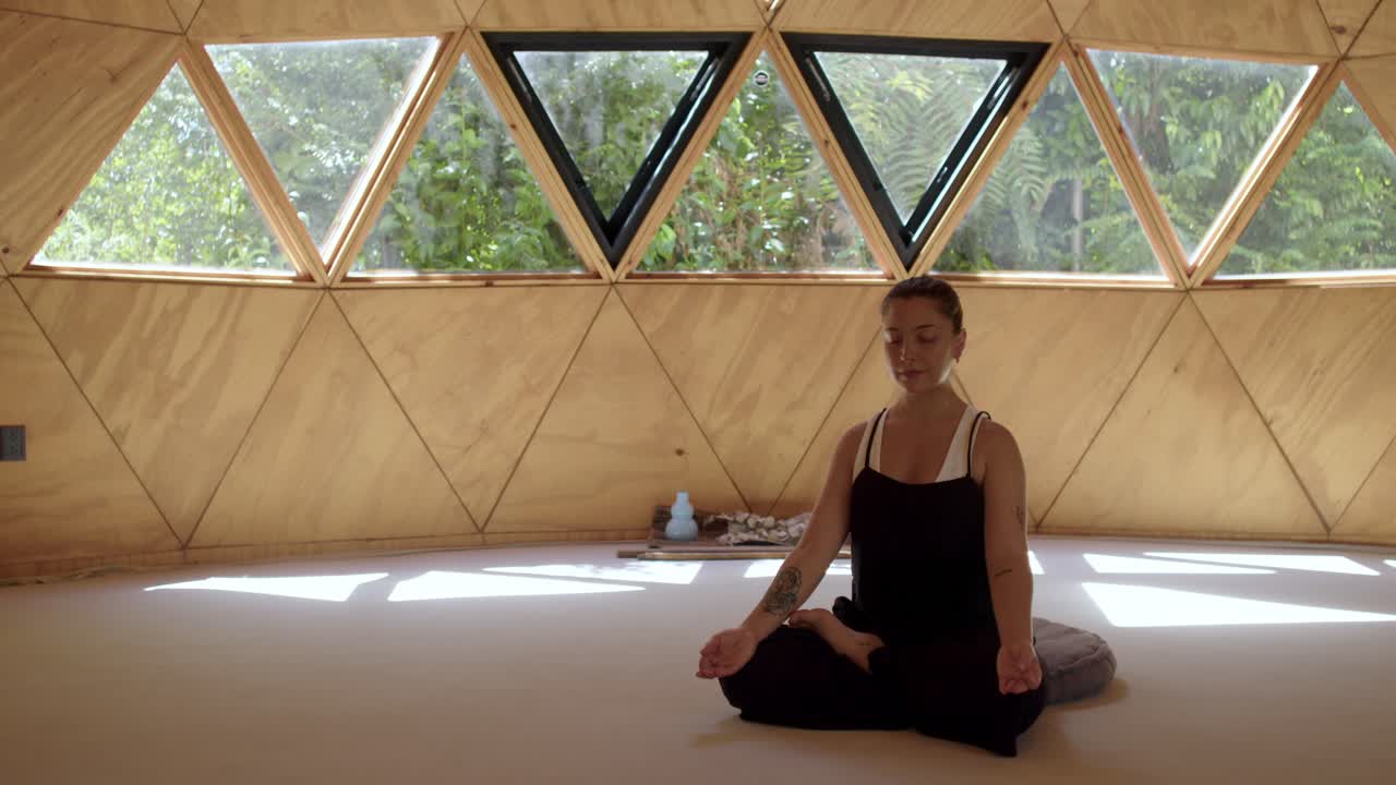 молодая женщина практикует йогу в спокойной геометрической студии, в окружении природы и спокойствия, бутылка с водой и учебные пособия позади