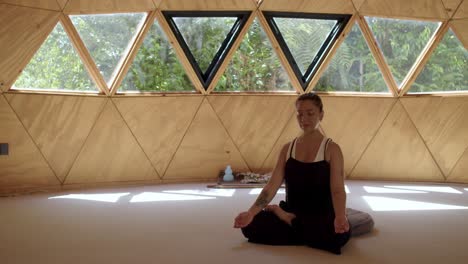 joven practicando yoga en un estudio geométrico tranquilo, rodeada de naturaleza y serenidad, botella de agua y suministros de estudio detrás