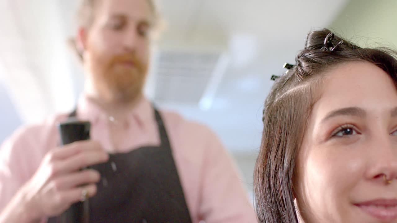 Caucasian male hairdresser spraying happy female client's hair with water at salon, slow motion