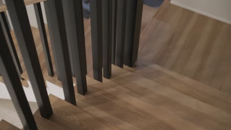 a top-down view of modern wooden stairs with black vertical balusters, showcasing the contrast of natural wood against a minimalist white background