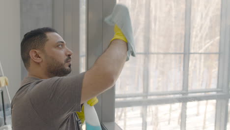 close up view of arabic cleaning man cleaning the window panes with a rag and glass cleaner inside an office