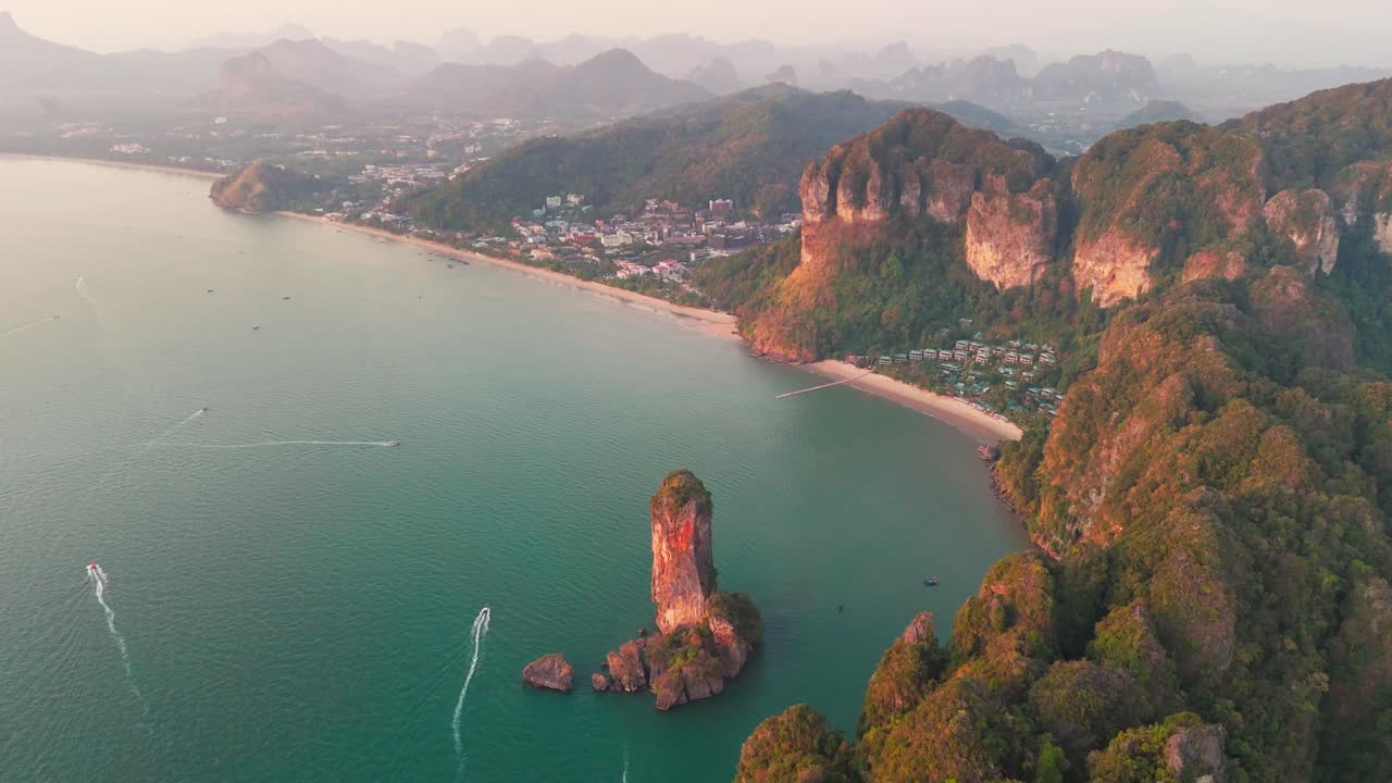 Aerial pullback above Nang Beach, Krabi, Thailand, with limestone cliffs and turquoise waters as boats drive in ocean at sunset