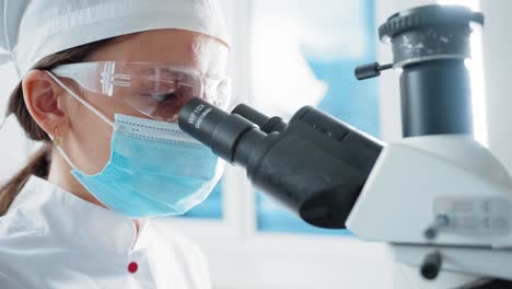 woman looking through microscope in lab
