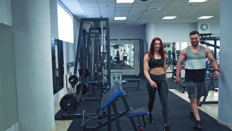 muscular man and attractive woman in sports club. modern background of fitness center and a happy couple coming to do their workout.