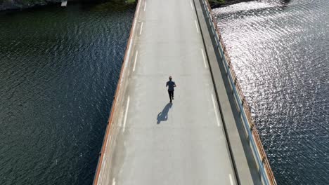 sun glistens on water as man jogs on bridge over norway fjord