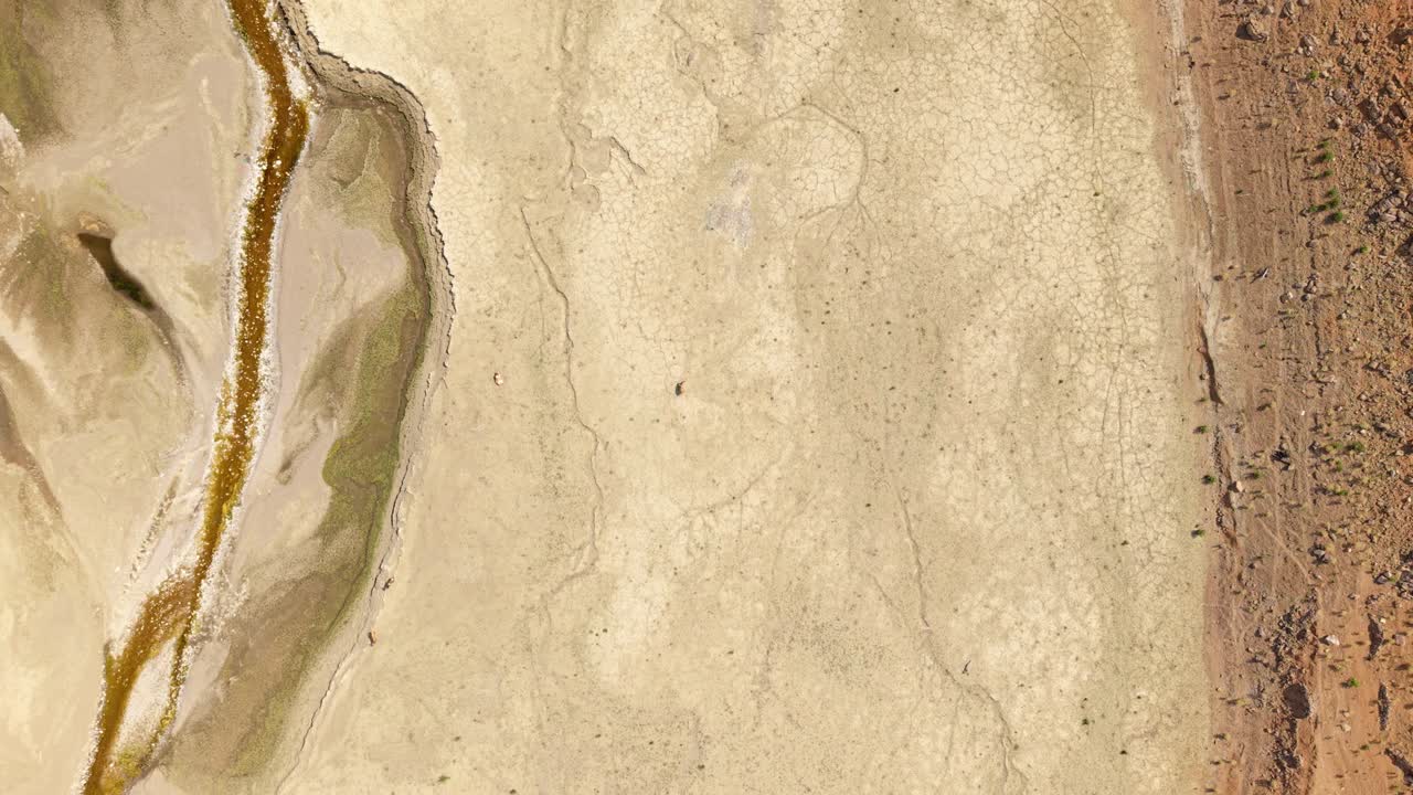 Topdown aerial of vast empty lakebed with a single figure walking across dry expanse