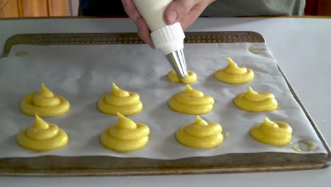 baker uses piping bag to pipe choux paste on baking tray