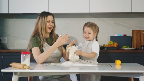 niña con madre amasa la masa cruda en la mesa en la cocina