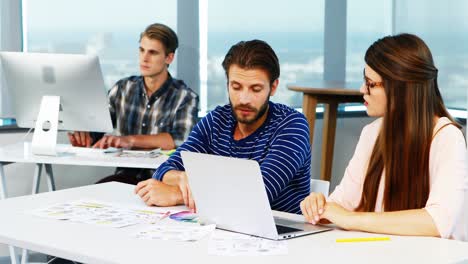 diseñadores gráficos discutiendo sobre una computadora portátil en el escritorio