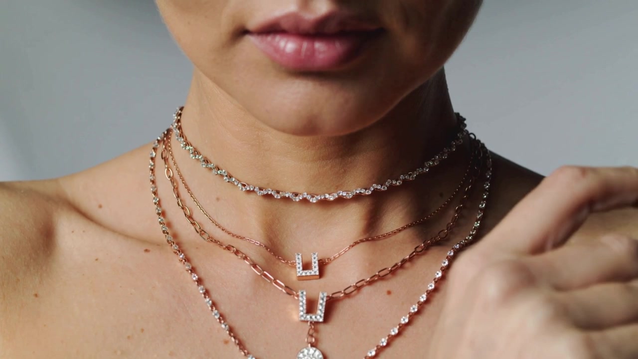 Model løfter håndleddet ved halsen, roterer og viser choker-kæder, rosenforgyldt armbånd i studie, bare skuldre