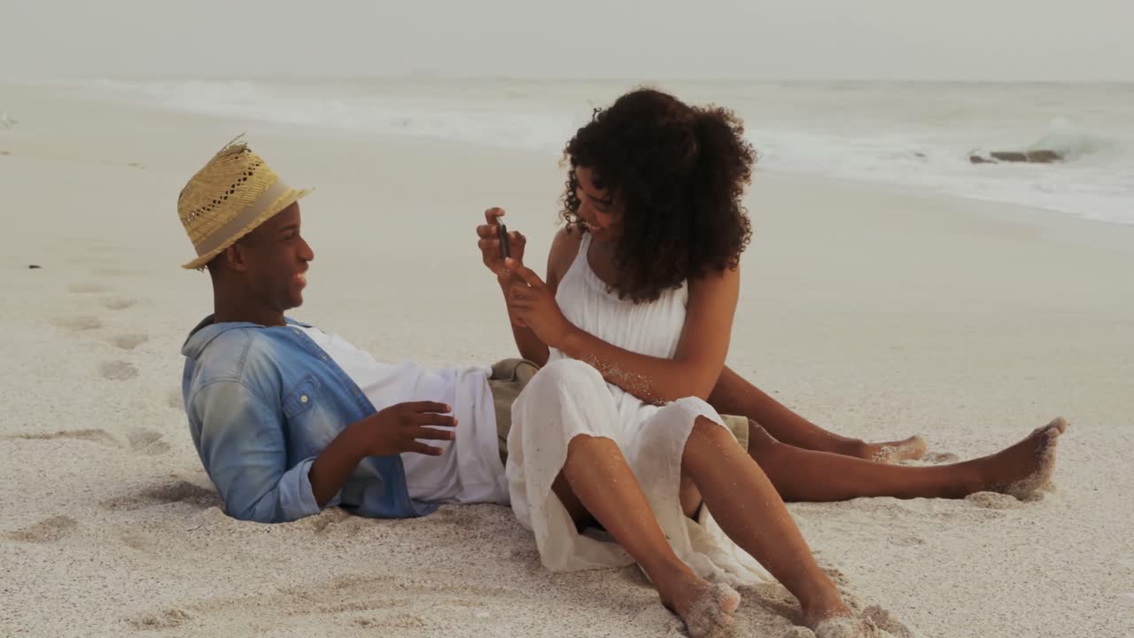 African American woman clicking photo of man with mobile phone on the beach 4k