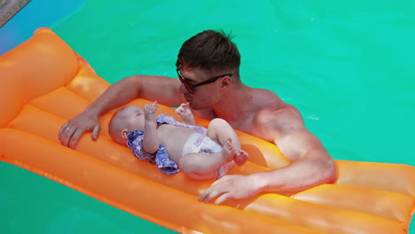caucasian man standing in the swimming pool. tiny infant boy lies on the inflatable mattress crying. top view.