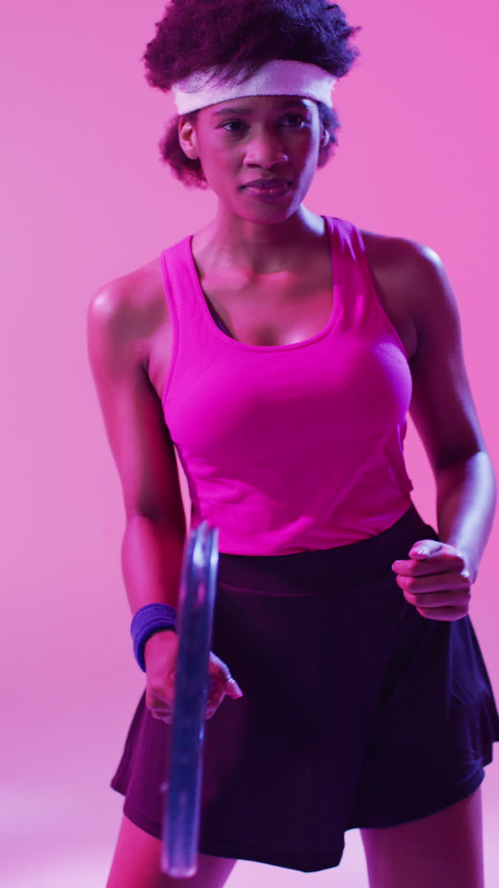 video vertical de una tenista afroamericana golpeando la pelota en un fondo rosa neón