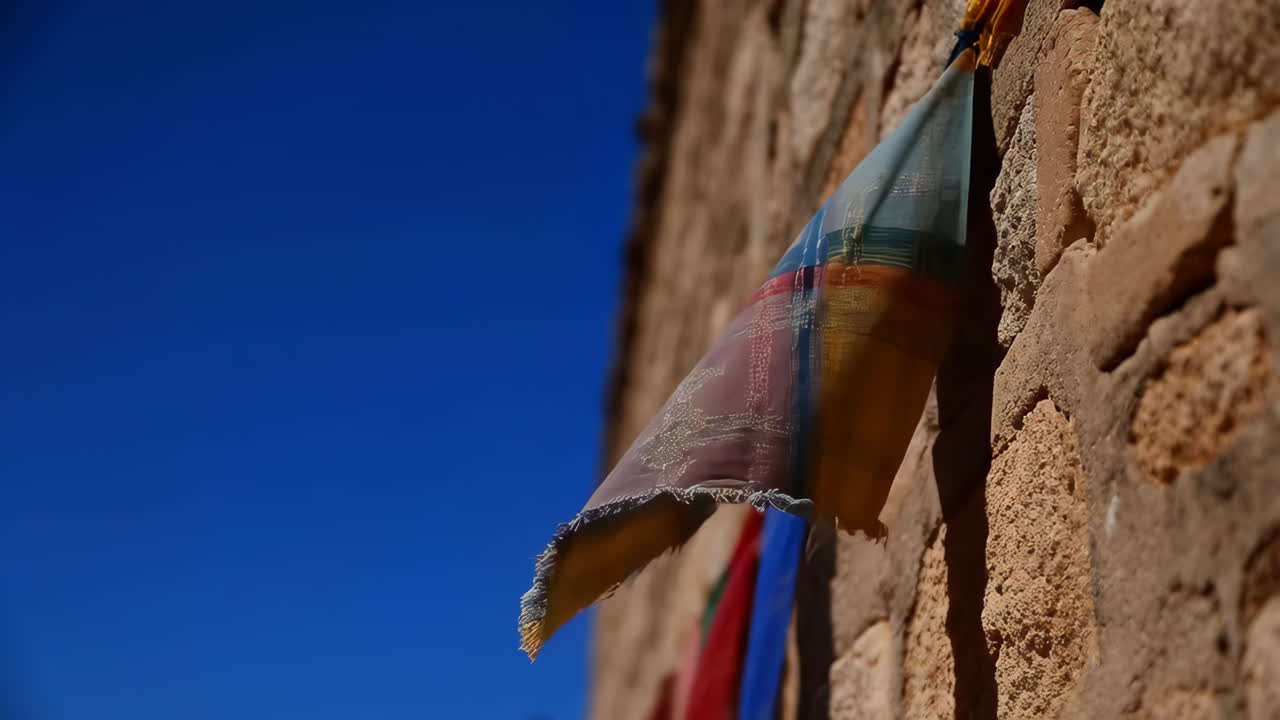 Colorful Flag Hanging on a Rustic Stone Wall Against a Blue Sky