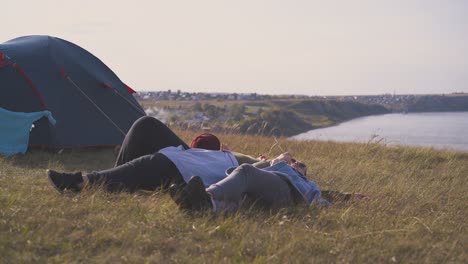 woman-friends-rest-lying-on-dry-grass-by-tent-on-river-bank