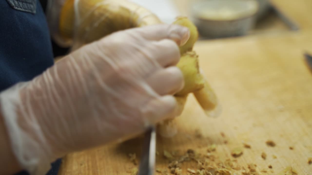 This is another over angle of a cook peeling the skin off of a ginger root.