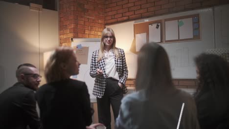 female manager presents new project plan to colleagues at meeting, explaining ideas on flipchart to coworkers in office, businesswoman gives presentation