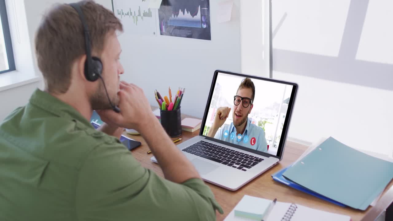 Kaukasisk mand bruger bærbar computer og telefonheadset på videoopkald med en mandlig kollega.