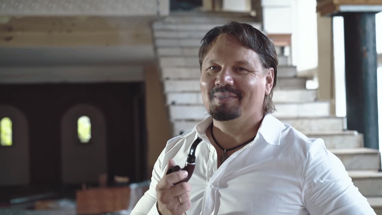 retrato de un joven brutal con barba que sonríe y fuma una pipa en primer plano