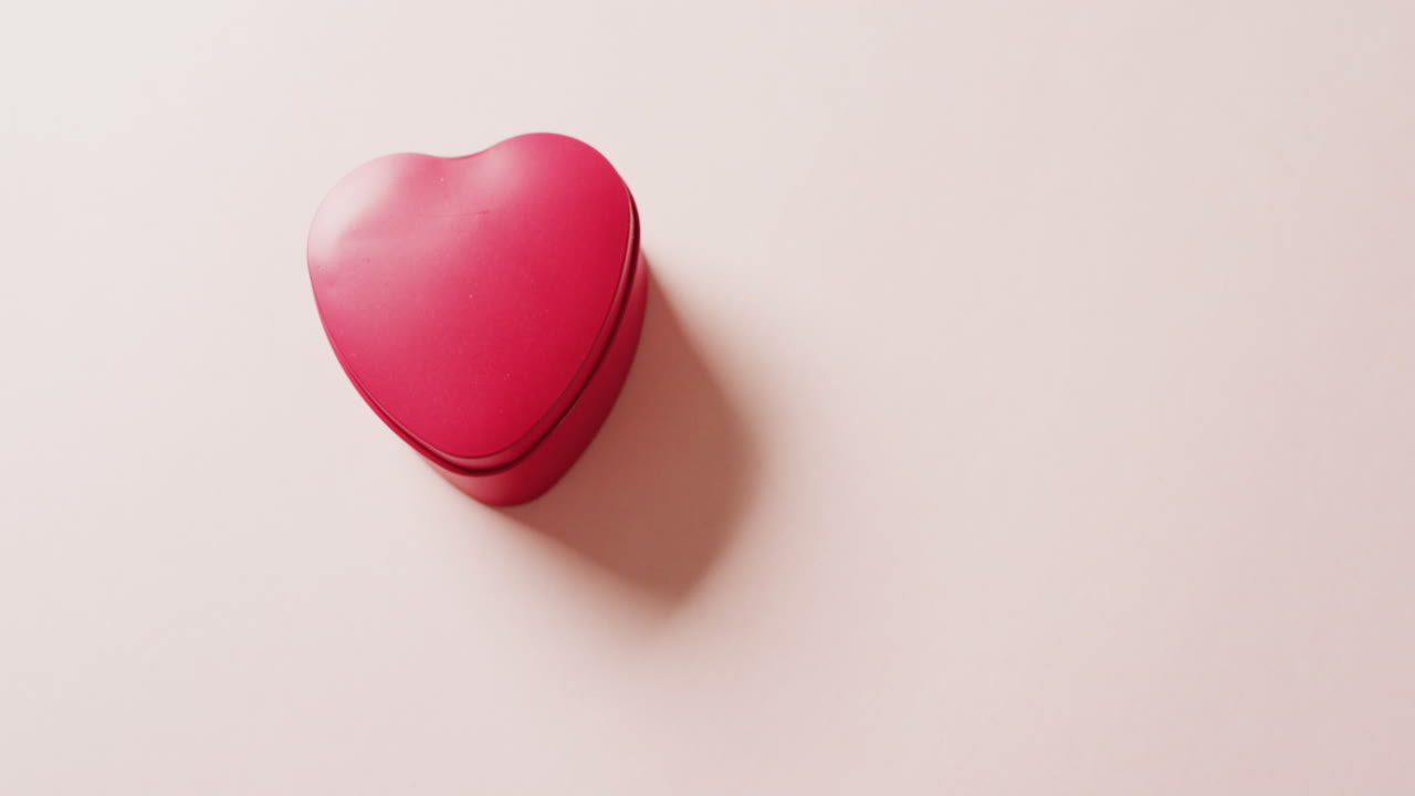 Video cenital de una caja roja en forma de corazón sobre fondo rosa, con espacio para texto.