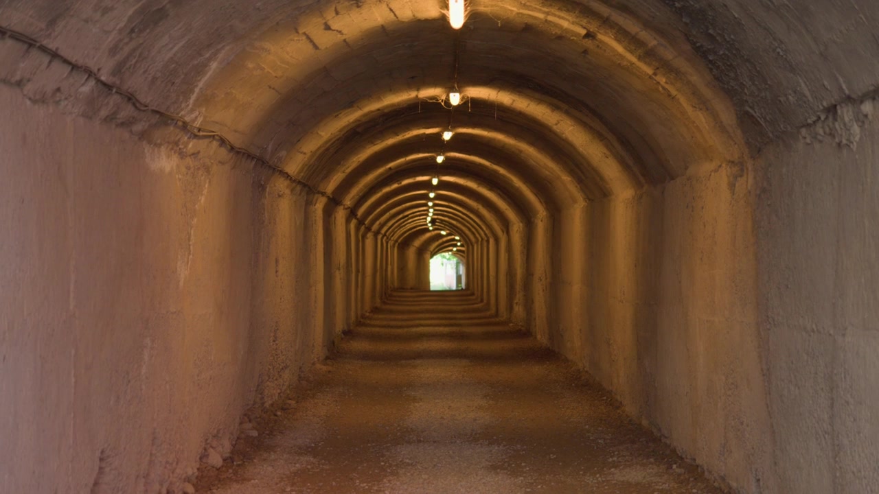 A symmetric perspective view of a lit concrete tunnel path leading toward a bright outdoor exit.