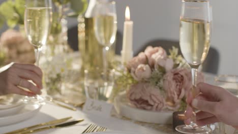 close up of couple making toast with champagne at table set for meal at wedding reception