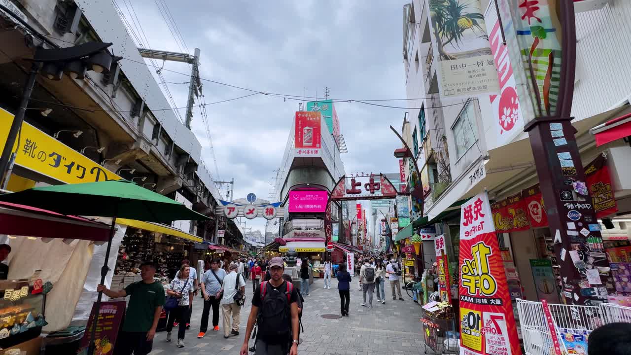 Crowded street in a busy outdoor market with vibrant shops and people walking under cloudy skies