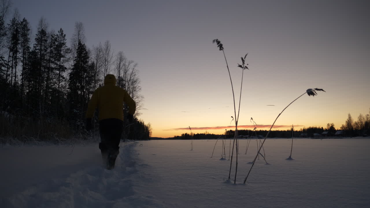 el hombre camina a través de la nieve hacia la puesta de sol de invierno, tiro estático