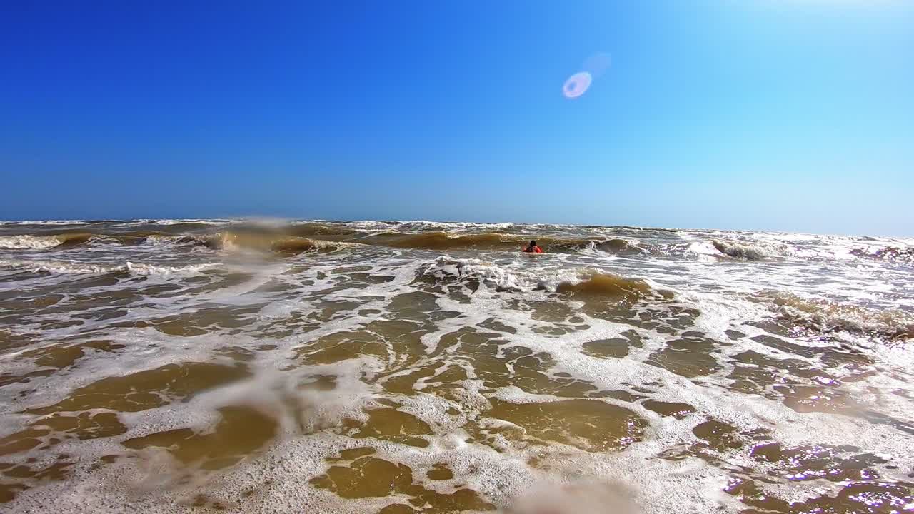 White foam on the dirty sea water. Big waves breaking on the shore. Happy child is having fun in the sea in summer.