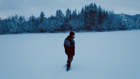 long-haired caucasian man is walking through snowscape near forest