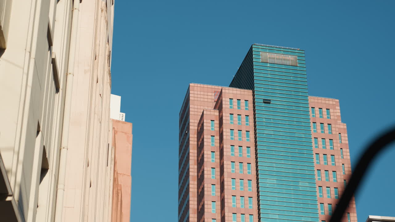 Grattacielo blu risplende. Paesaggio urbano di mezzogiorno con vibrante struttura turchese tra edifici neutri. Moderna torre illuminata dal sole con finestre geometriche tra semplici strutture beige in una strada stretta